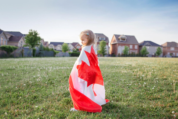 Criança envolta na bandeira do Canadá em um campo verde
 Criança envolta na bandeira do Canadá em um campo verde
