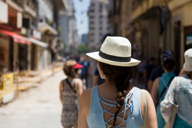 Mulher com chapéu de palha caminhando em uma rua movimentada, observando o ambiente urbano
