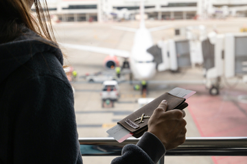 Pessoa segurando bilhetes de embarque em um aeroporto, com vista para um avião e equipe de solo ao fundo.
 Pessoa segurando bilhetes de embarque em um aeroporto, com vista para um avião e equipe de solo ao fundo.